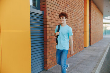 Smiling teen boy with red hair walks past a brick wall in city street