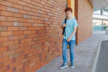 Teenage boy with backpack smiling while walking by brick wall
