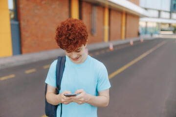 Teen boy texting outdoors with joyful smile near school building