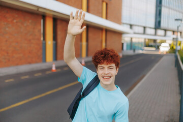 Smiling redhead teen boy waves outside in urban school zone