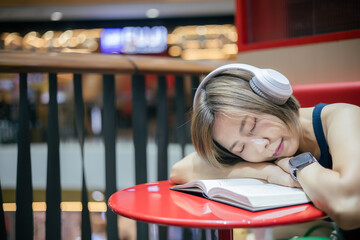 Woman is sleeping while reading a book in a coffee shop in a shopping mall