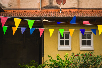 Colorful festive banners sway gently under a sunny sky, bringing cheer to a quaint courtyard...