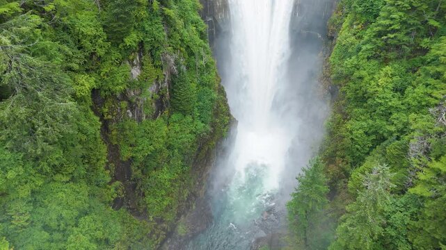 Aerial view of water cascading from a dam, contrasting against the dark, still reservoir and lush green trees, Sitka, Alaska, United States.