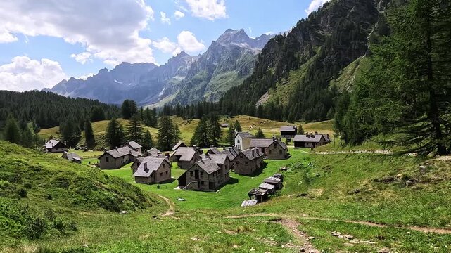 Traditional alpine houses in Crampiolo sit among meadows and peaks in Alpe Devero, Piedmont, Italy, under a sunny summer sky.