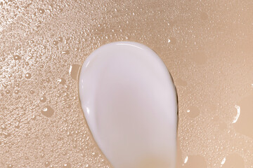 creamy white texture smear sample on light beige background with water drops close up