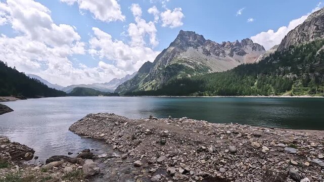 Rocky lakefront view of Lago di D&eacute;vero with forested slopes and rugged peaks beneath a partly cloudy sky.