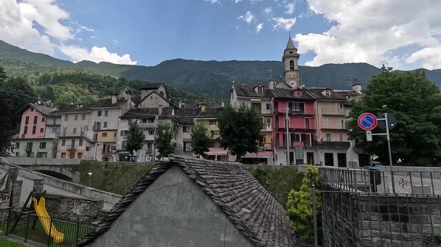 Colorful buildings and stone rooftops in the alpine town of Varzo, with a church bell tower and mountain backdrop in Piedmont, Italy.