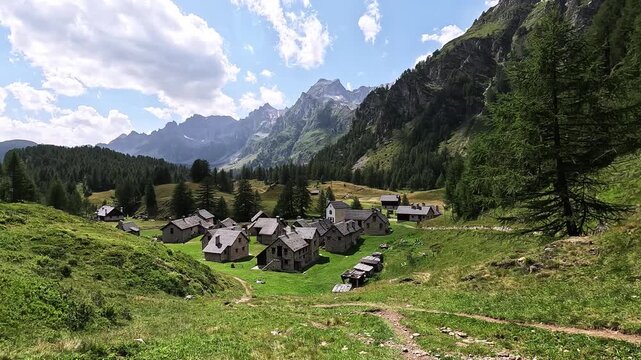 Traditional alpine houses in Crampiolo sit among meadows and peaks in Alpe Devero, Piedmont, Italy, under a sunny summer sky.