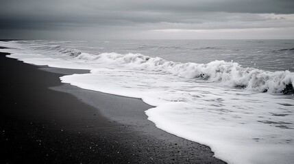 Dark sand beach meets foamy waves on a gray overcast day