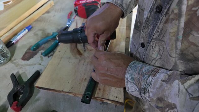 Man hands used a cordless drill with LED light to make a hole in metal rod