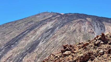 The stunning scenery includes a majestic volcanic mountain and rocky terrain under a clear blue sky