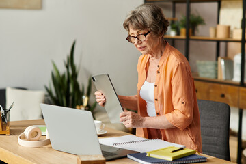 Senior woman enjoying a cozy moment at home while using a tablet and working at a desk