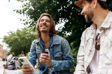 Two male mates chilling outside in public park talking to each other, having fun, joking, discussing funny situations, gossiping, sharing latest news, life hacks, trends, plans for future