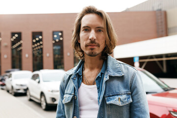 Male car trader or dealer posing against auto park and looking at camera. Hipster salesman looking for clients to distribute new vehicles, sharing life hacks on choosing reliable transport