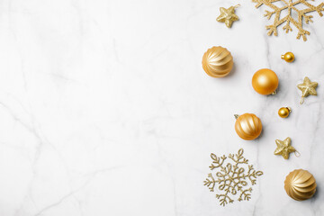 Festive arrangement of gold Christmas ornaments and decorations on a white marble surface with copy...