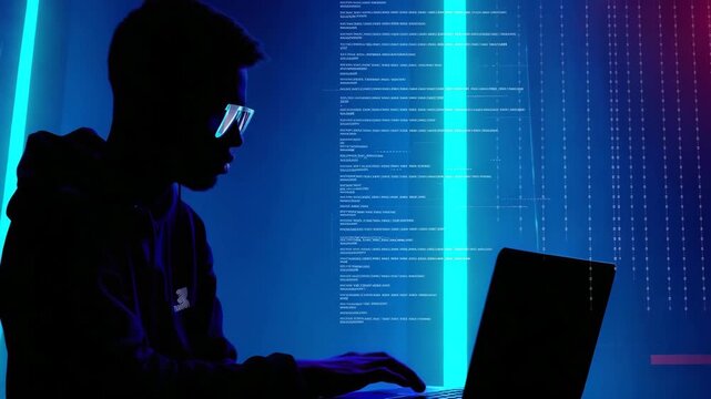 Young male hacker working on laptop in dark room. Black guy programmer in glasses coding at night with neon blue light. Network security, digital technology concept footage