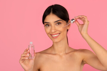 Smiling young woman applying face serum with dropper. Fresh skincare moment promoting hydration and...