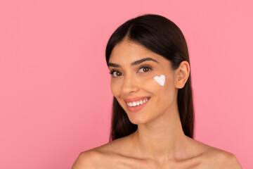 Happy young woman with heart shaped cream dot on cheek. Symbolizing love, self care and skincare...