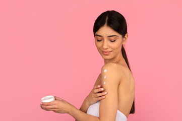 Woman gently applying body cream dots on shoulder. Soft beauty and skincare ritual in pastel studio background for moisturizing and selfcare concept, copy space