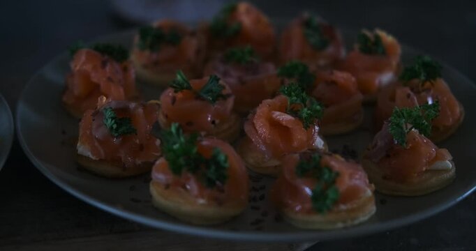 Close-up of small appetizers for a festive table with salmon and greens. Cream cheese is spread on a pancake and salted salmon is lying on it. Serving dishes on a festive table.