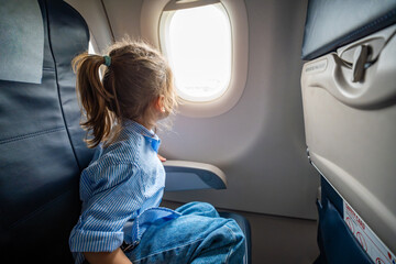 Little girl looking out the airplane window during a flight. Wonder, travel experience, and childhood curiosity in the air.