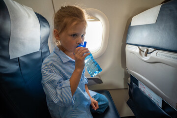 Little girl drinking water from a plastic bottle during a flight. In-flight hydration, travel routine, and caring for body needs while flying