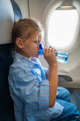 Little girl drinking water from a plastic bottle during a flight. In-flight hydration, travel routine, and caring for body needs while flying