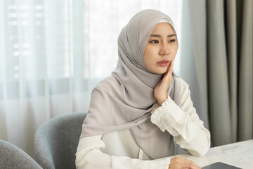 Muslim woman in hijab touching cheek with painful expression at home, concept of toothache or...