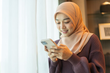 Asian muslim woman use smartphone at home, female in hijab checking messages, modern communication,...