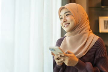 Asian muslim woman use smartphone at home, female in hijab checking messages, modern communication,...