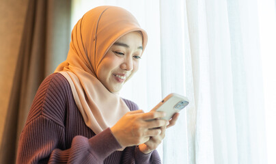 Asian muslim woman use smartphone at home, female in hijab checking messages, modern communication,...