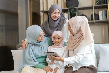 Muslim family four generations sitting on sofa enjoying tablet, joyful moment with grandmother,...