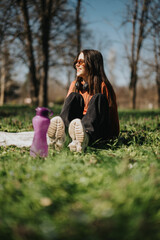 Young woman enjoying a sunny day sitting outdoors in a park surrounded by nature, with beverages...