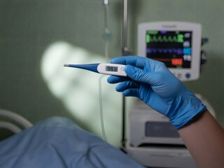 Photo of a hand in a blue glove holds a thermometer displaying a normal temperature