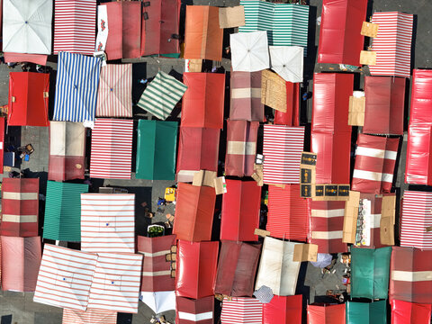 Aerial view of vibrant market stalls creating a colorful mosaic with striking red, green, and white canopies in Piazza della Repubblica, Torino, Piemonte, Italy.