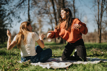 Two young women bond and laugh together during a sunny day at the park, showcasing friendship and...