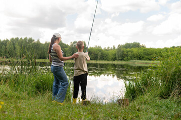 Mother and teenage son fishing together on lake shore, enjoying summer day in nature