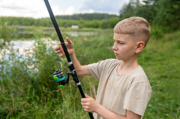 Teenage boy learning to cast fishing rod on lake shore, enjoying outdoor summer activity