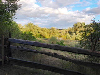Scenic countryside landscape with a rustic wooden fence in the foreground and a sunlit river valley...
