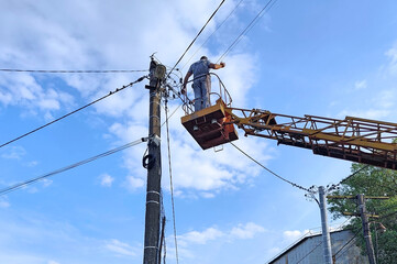 Electrician working at height on a power line from a lift platform against a blue sky with...