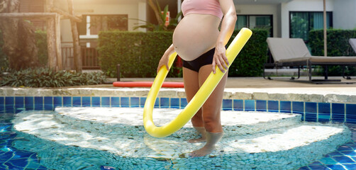 Pregnant young woman about to do exercises in pool with foam swim noodles