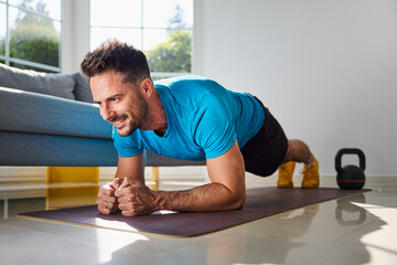 Smiling mid adult man doing plank exercise during home workout