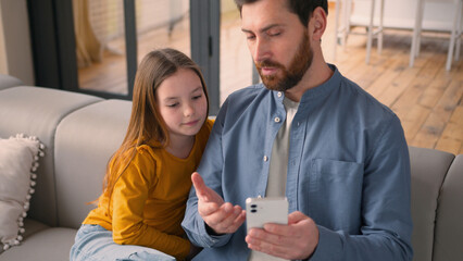 Happy family smiling Caucasian man guy dad talk to little girl at home daddy male parent teaching daughter kid use mobile phone device father child ordering food online browsing network social media