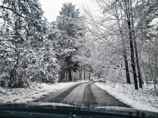 Driving on curvy road through winter forest. A narrow road in snowy forest, surrounded by pine...