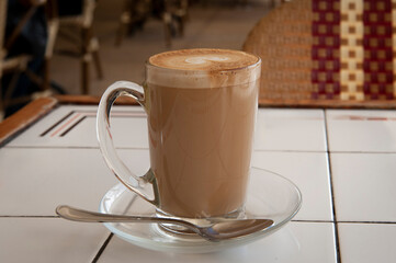Freshly brewed cup of hot, foamy cappuccino with decorative milk froth topping in a tall, glass mug...