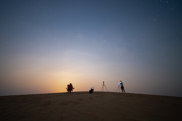 Fototapeta premium Couple camping in the desert taking photo and relax over the sand dune desert with moon light