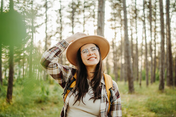 Young caucasian woman hiking or trekking through scenic forest with hiking sticks during golden hour