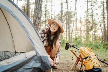 Young caucasian woman preparing tent and campfire in the scenic forest during golden hour