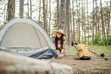 Young caucasian woman preparing tent and campfire in the scenic forest during golden hour
