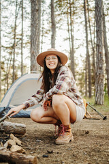 Young caucasian woman preparing tent and campfire in the scenic forest during golden hour